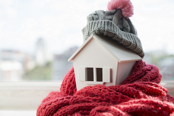 house in winter - heating system concept and cold snowy weather with model of a house wearing a knitted cap