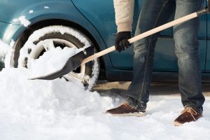 man shoveling snow out the wheel of his car